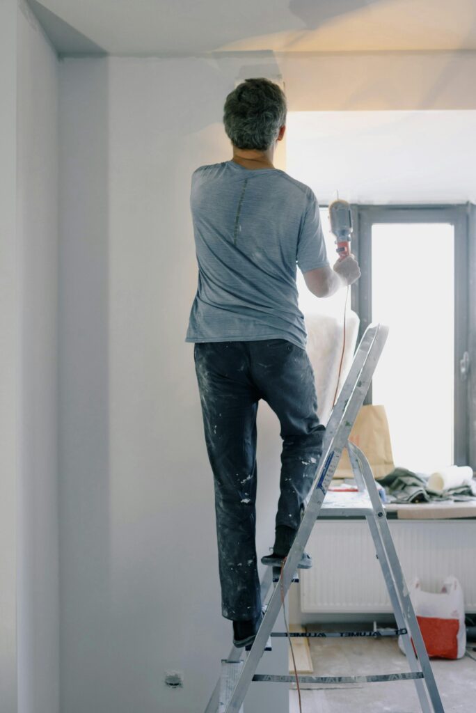 A man stands on a ladder using an electric tool for home renovation in a well-lit interior space.