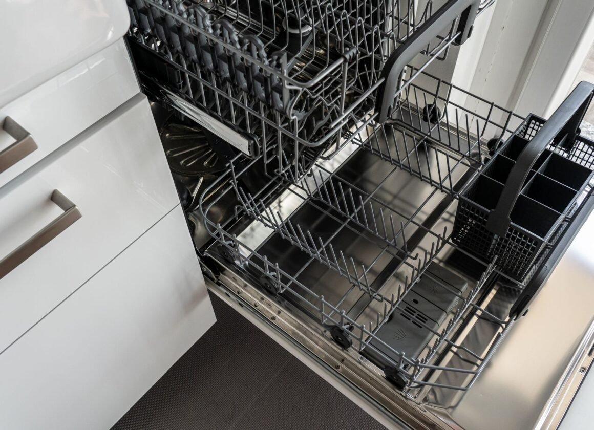 A clean and empty stainless steel dishwasher open in a modern kitchen setting.
